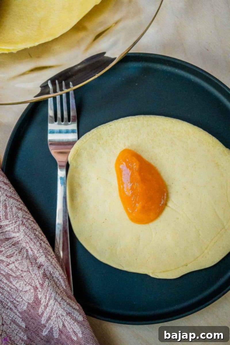 Delicate Apricot Crepes 5 Adding a generous tablespoon of smooth apricot jam onto the center of a thin pancake (Palatschinke).
