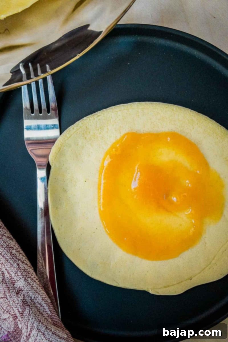 Delicate Apricot Crepes 6 Spreading fine apricot jam evenly across the surface of a thin pancake (Palatschinke) before rolling.