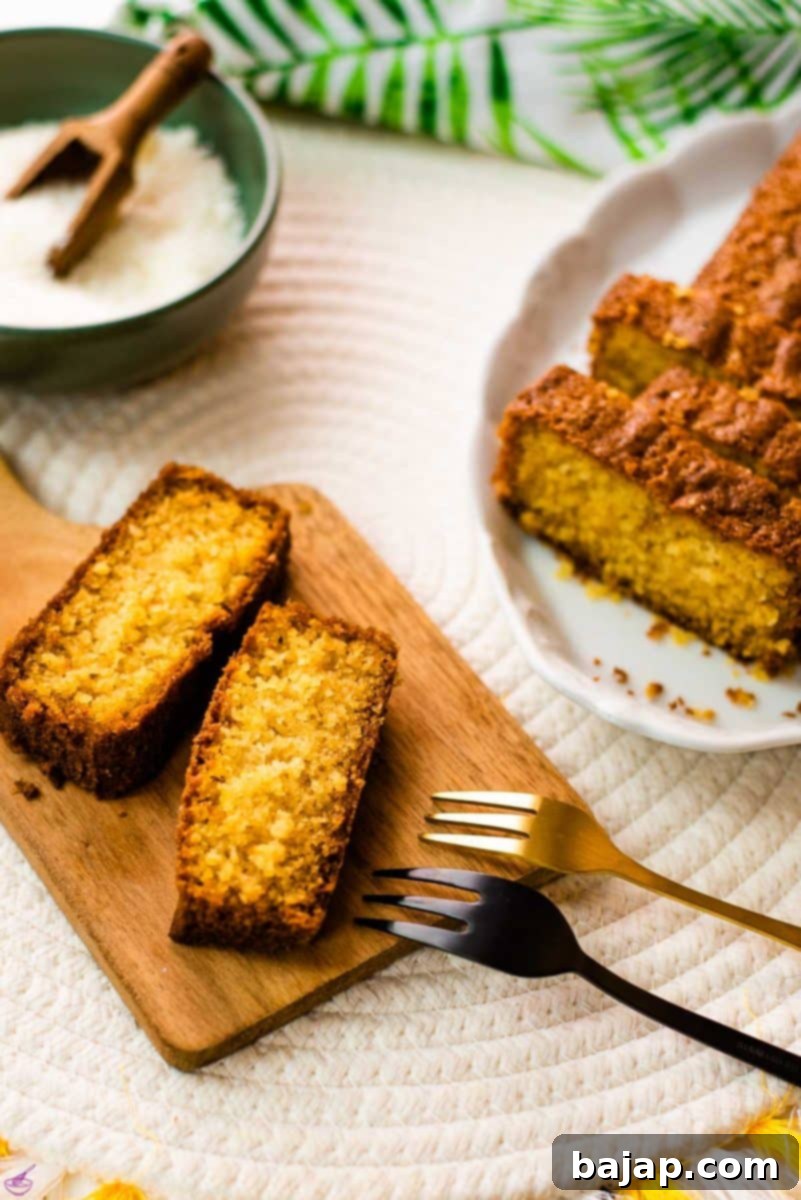 Two slices of golden-brown coconut pound cake resting on a rustic wooden board. In the soft-focus background, a small bowl of white coconut flakes and another slice of the pound cake are visible, hinting at the delicious texture and tropical flavor.