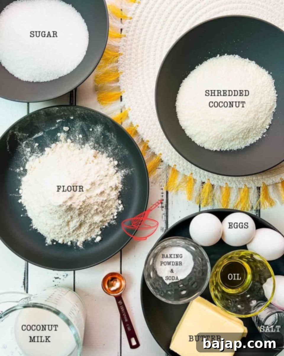 A selection of fresh and dry ingredients laid out on a wooden surface, including shredded coconut, coconut milk, butter, eggs, flour, and sugar, all ready to be used to make the delicious coconut pound cake.