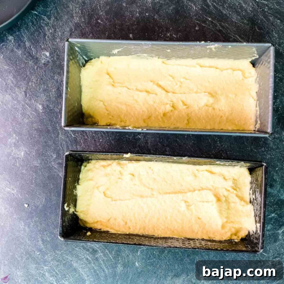 Pouring the creamy coconut pound cake batter evenly into two small loaf pans, ready for the oven. The smooth texture of the batter promises a moist finished cake.