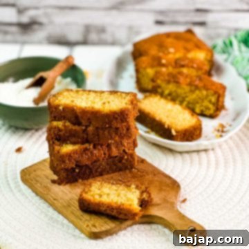 Lovely stacked layers of coconut pound cake on a beautiful wooden board. In the background, you will find coconut flakes in a bowl and a sliced coconut pound cake.
