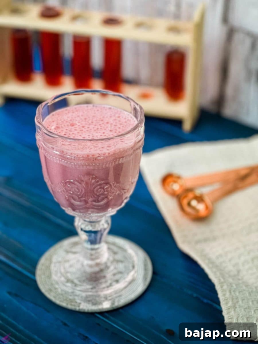 Cute and delicious pink strawberry milk in a gorgeous serving glass. Placed on a glass coaster on blue wooden ground.