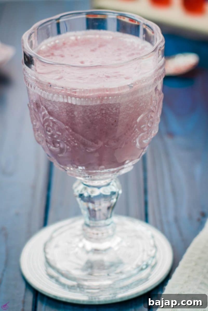 Cute and delicious pink strawberry milk in a gorgeous serving glass. Placed on a glass coaster on blue wooden ground.