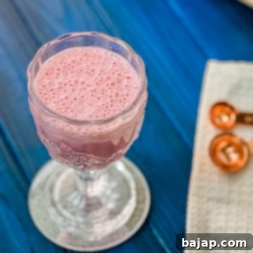 Cute and delicious pink strawberry milk in a gorgeous serving glass. Placed on a glass coaster on blue wooden ground.