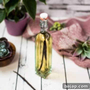 A beautiful bottle with amber-colored homemade vanilla vodka on a white wooden base.
