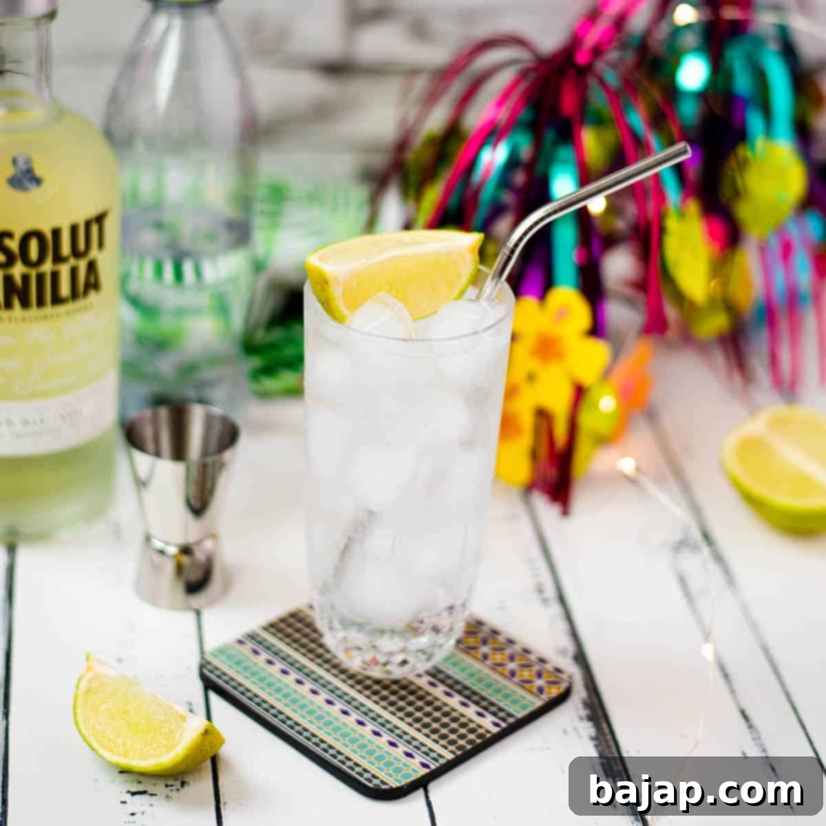 Beautiful glass filled with vanilla vodka tonic, on colorful coaster placed on white wooden board.