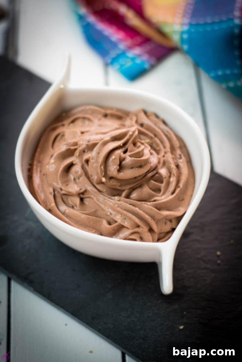 A beautifully presented serving of dark chocolate pudding, piped into a white ceramic bowl and resting on a black slate plate, ready for garnishing and enjoyment.