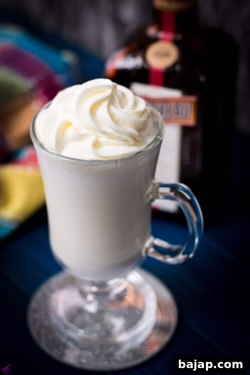 Delicious white Cointreau (orange liqueur) milkshake, garnished with orange zest, for adults on a stylish mirror glass coaster and a dark blue wooden base.