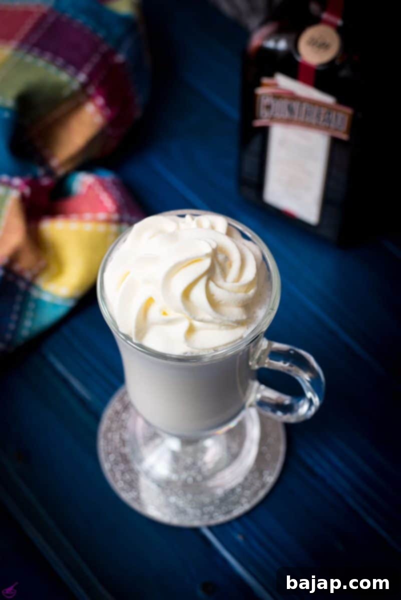 A perfectly blended white Cointreau (orange liqueur) milkshake for adults, served in an elegant glass on a mirror coaster, set against a dark blue background, ready to be enjoyed.
