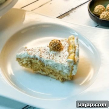 A beautiful slice of a delicious almond cream cake. Garnished with whipped cream, grated chocolate and a Giotto. Served on white plate on white wooden background.