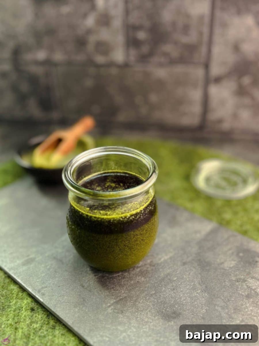Effortless Matcha Butter Recipe 8 A preserving jar filled with warm, liquid Matcha butter (before cooling) on a slate plate, showcasing its rich green color.