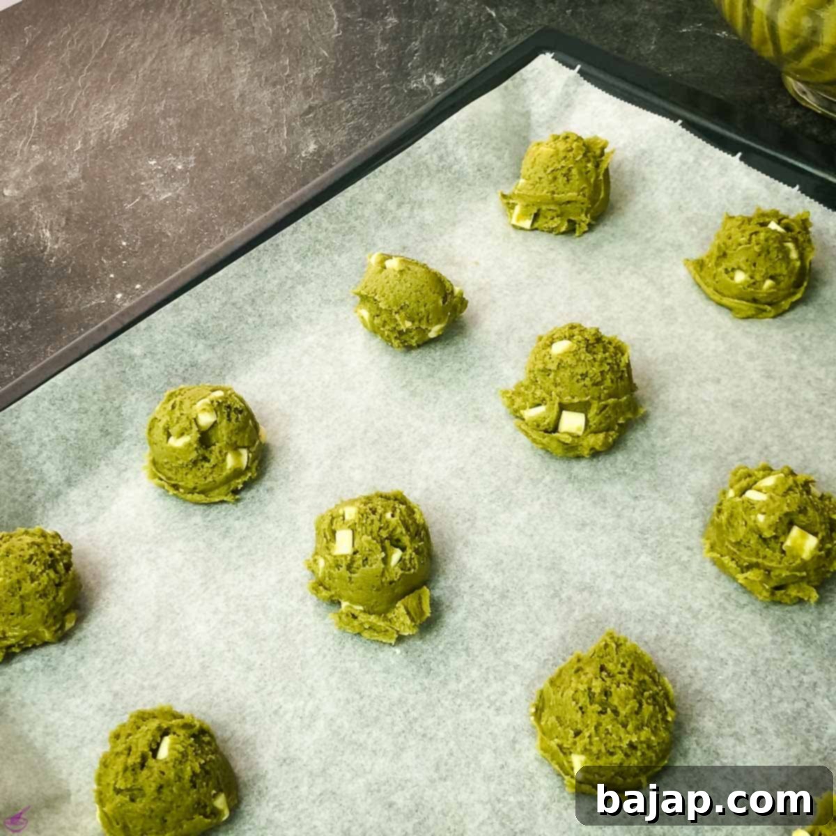 Rows of scooped Matcha cookie dough, evenly spaced on a baking sheet, ready for baking.