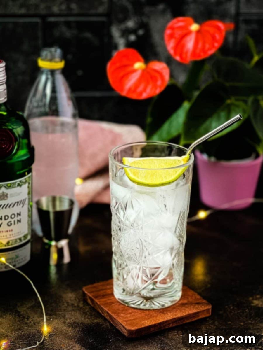 Highball glass filled with gin and tonic, garnished with lime, placed on wooden coaster.