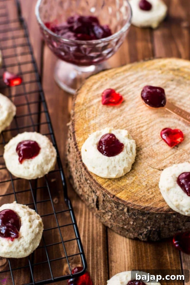 Gorgeous raspberry cream cheese thumbprint cookies on black cooling rack and wooden board.