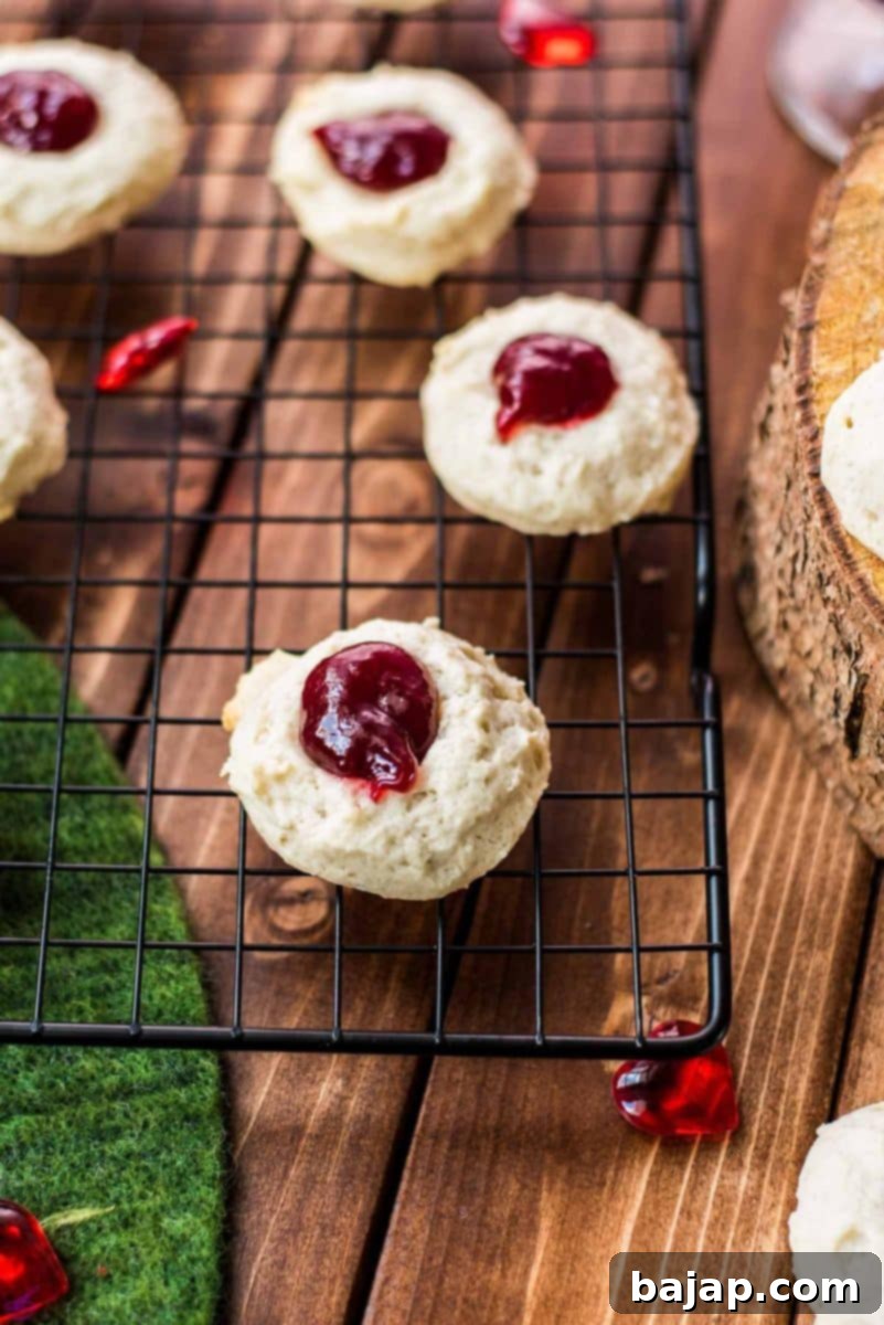 Gorgeous raspberry cream cheese thumbprint cookies on black cooling rack.