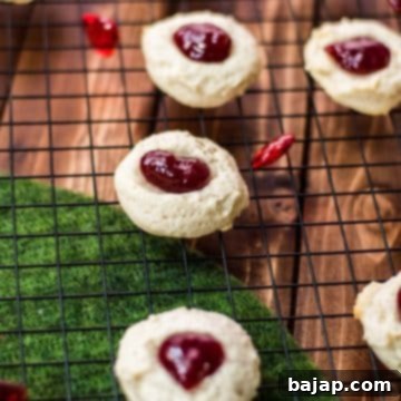 Gorgeous raspberry cream cheese thumbprint cookies on black cooling rack.