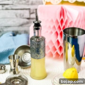 Bottle filled with freshly squeezed lemon juice fitted with a pouring spout, surrounded by cocktail making tools.
