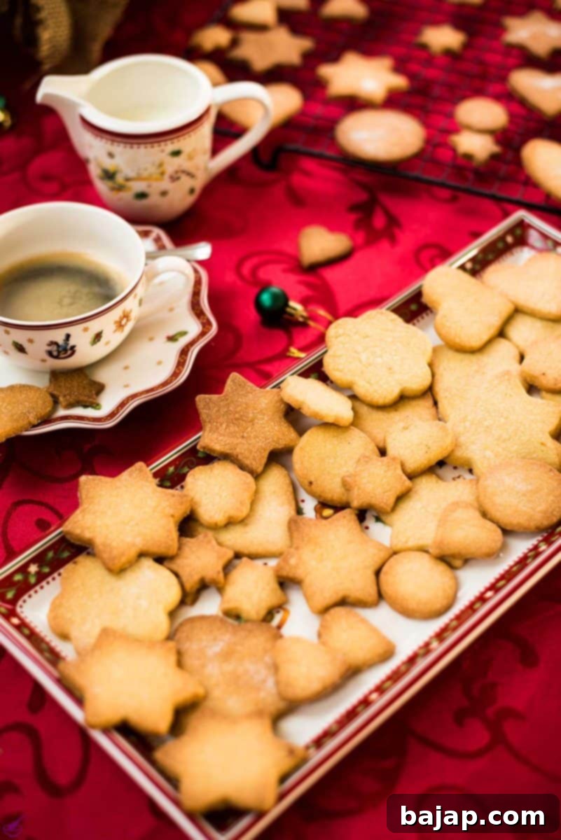 Delicious crispy sugar cookies on beautiful Christmas tray, placed on Christmassy red tablecloth.