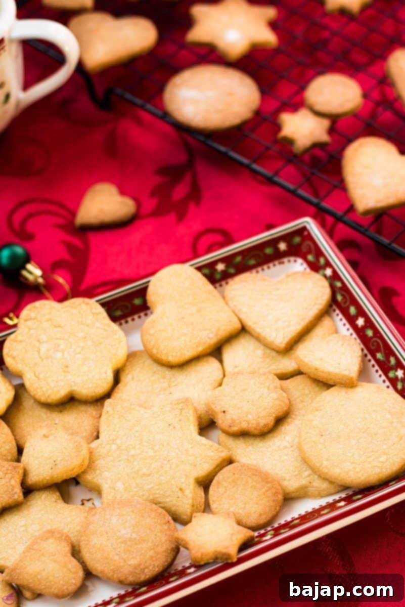 Delicious crispy sugar cookies on beautiful Christmas tray, placed on Christmassy red tablecloth.