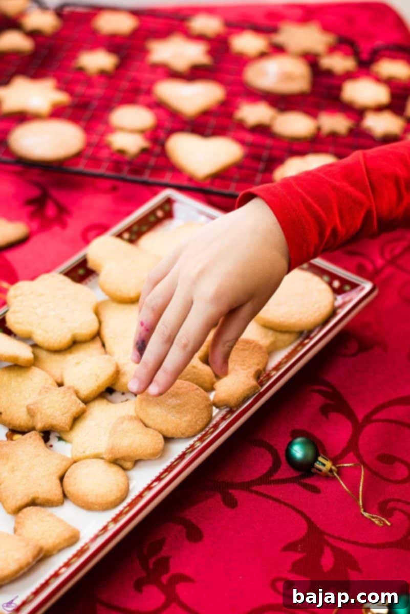 Delicious crispy sugar cookies on beautiful Christmas tray, placed on Christmassy red tablecloth.