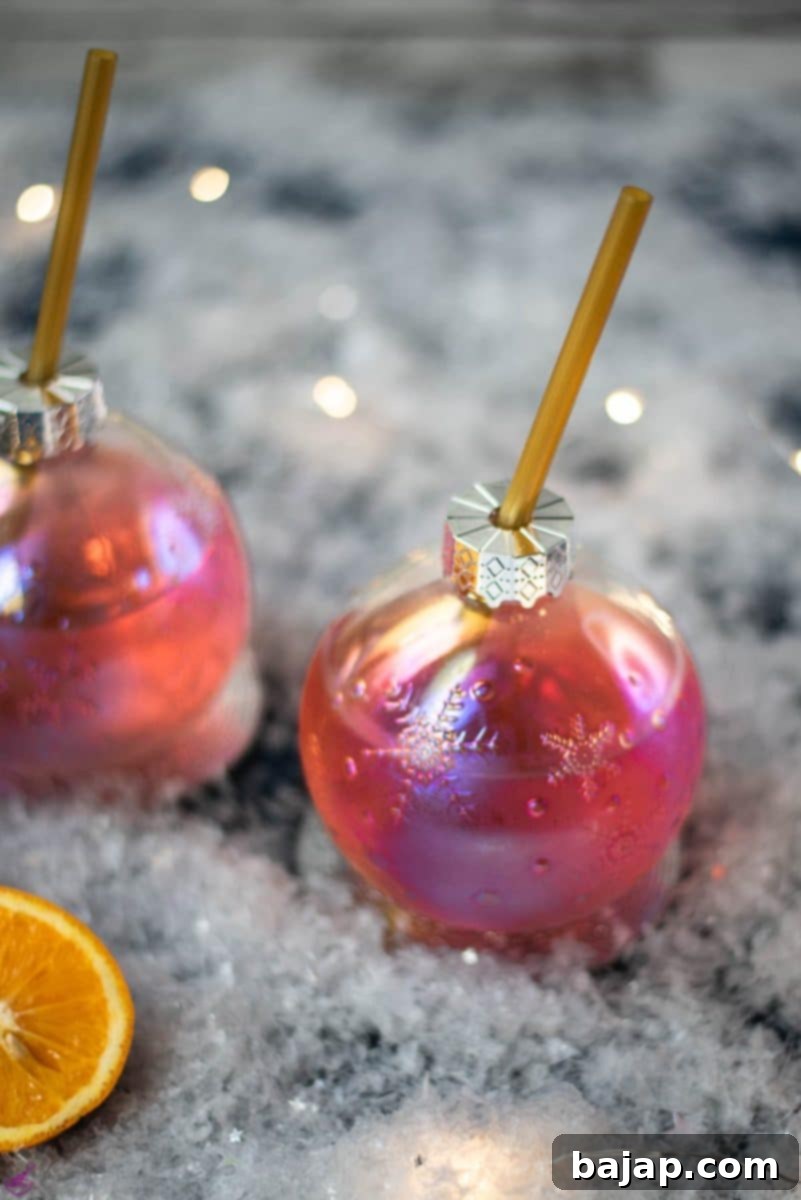 Gorgeous Christmas ornament shaped glass filled with festive cranberry gin tonic, garnished with an orange slice and rosemary.