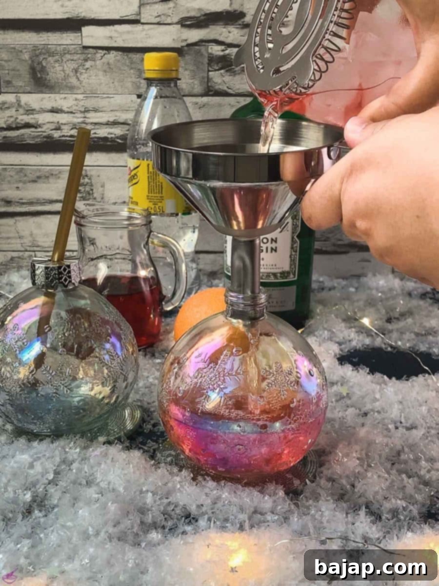Pour the prepared cranberry gin tonic into festive Christmas ornament shaped glasses using a funnel.
