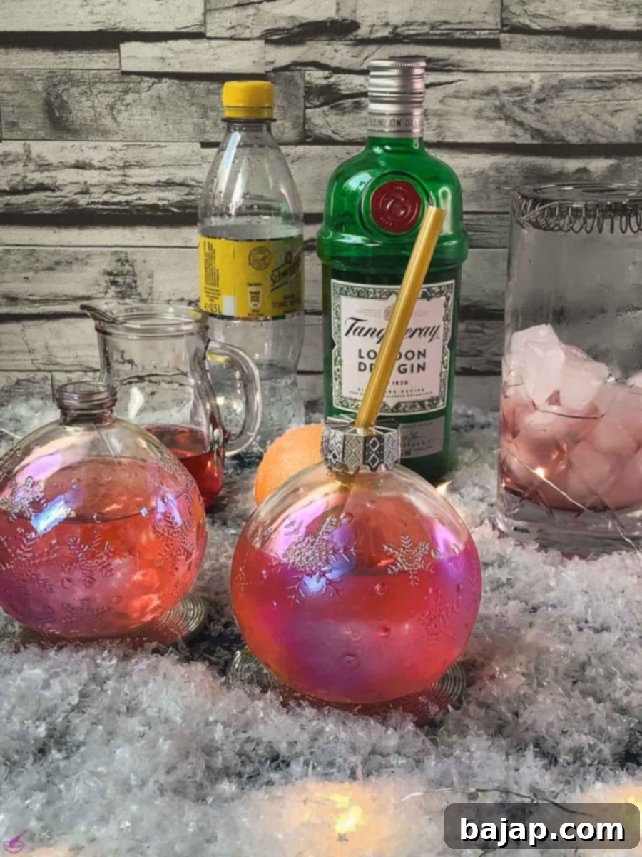 A stunning Christmas ornament shaped glass, filled with festive cranberry gin tonic, resting on a glass coaster, ready to be enjoyed.