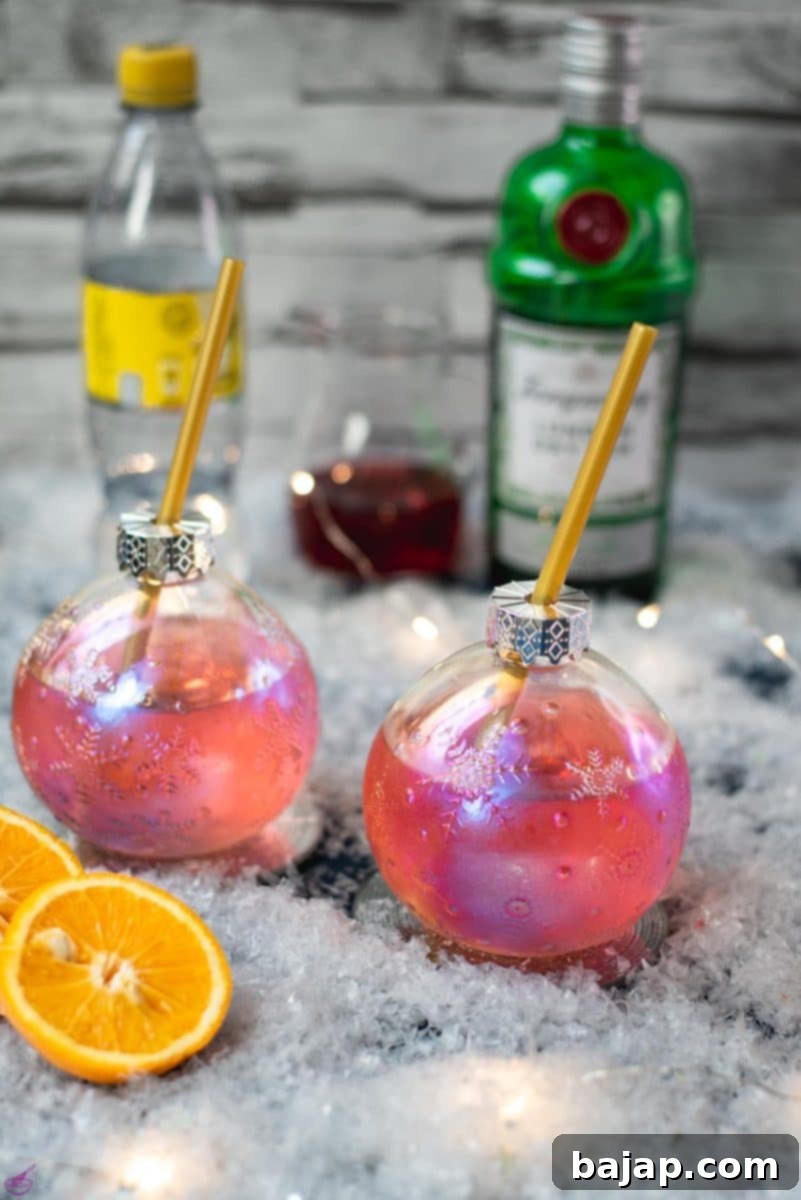 Gorgeous Christmas ornament shaped glass filled with festive cranberry gin tonic, placed on glass coaster.