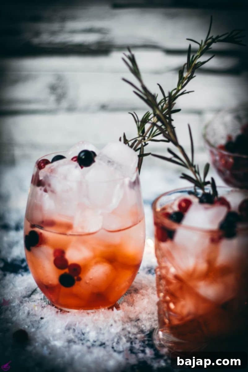 Two glasses filled with delicious cranberry Aperol spritz, placed on snowy ground, garnished with a delicious berry mix.