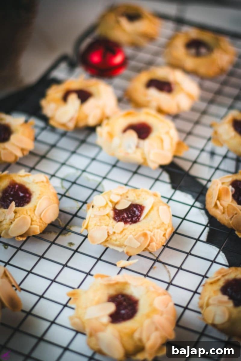 Delectable raspberry almond thumbprint cookies gracefully cooling on a wire rack, showcasing their perfect golden crust and vibrant jam filling.