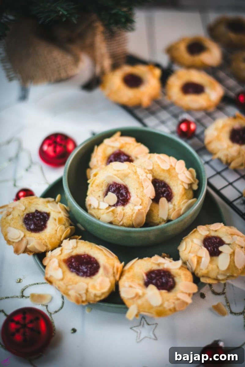 Delectable raspberry almond thumbprint cookies, beautifully presented in a green festive bowl, surrounded by twinkling red Christmas baubles, creating a joyful holiday atmosphere.