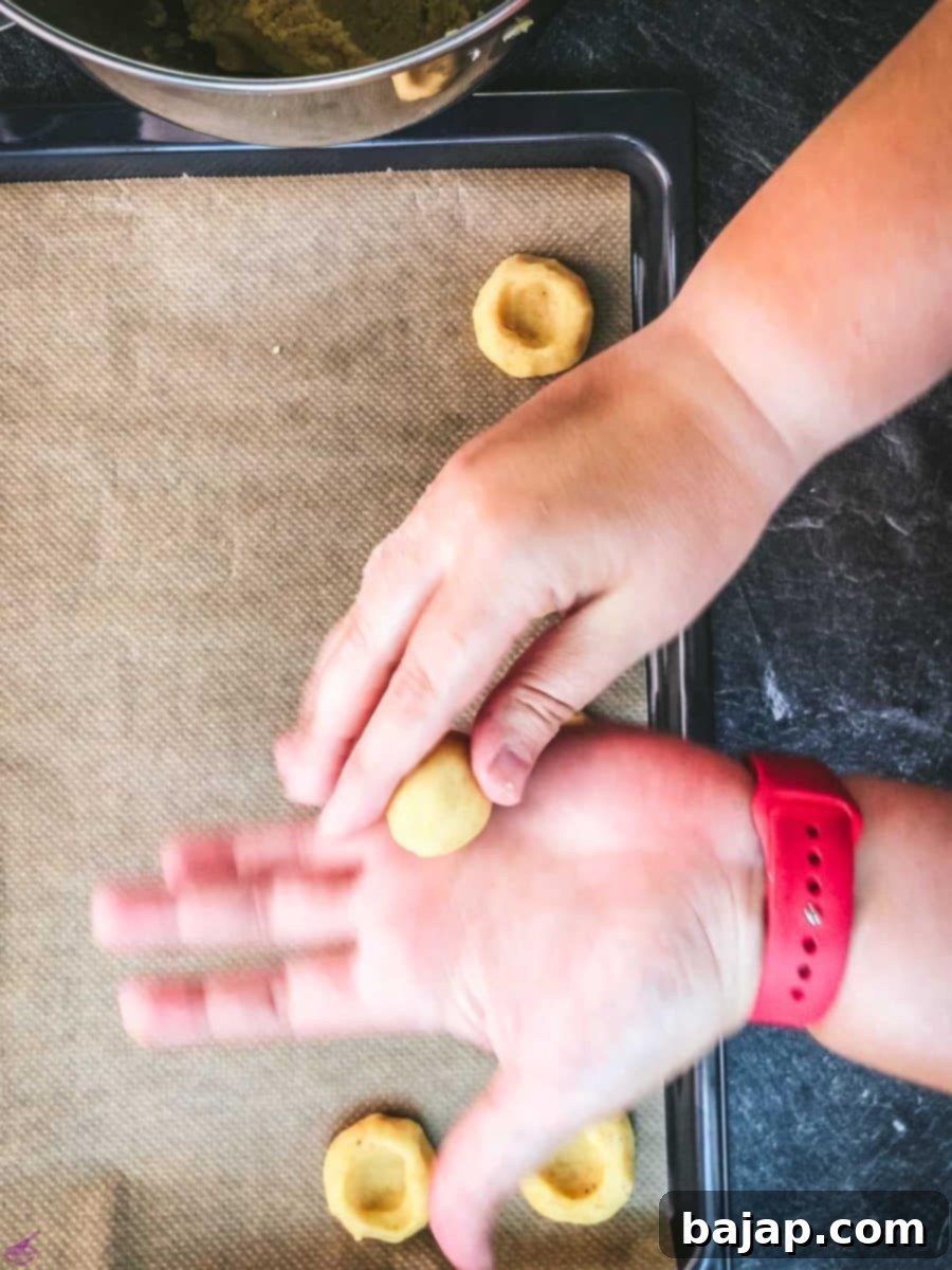 Rolling small portions of cookie dough into perfectly round balls before placing them on a baking sheet.