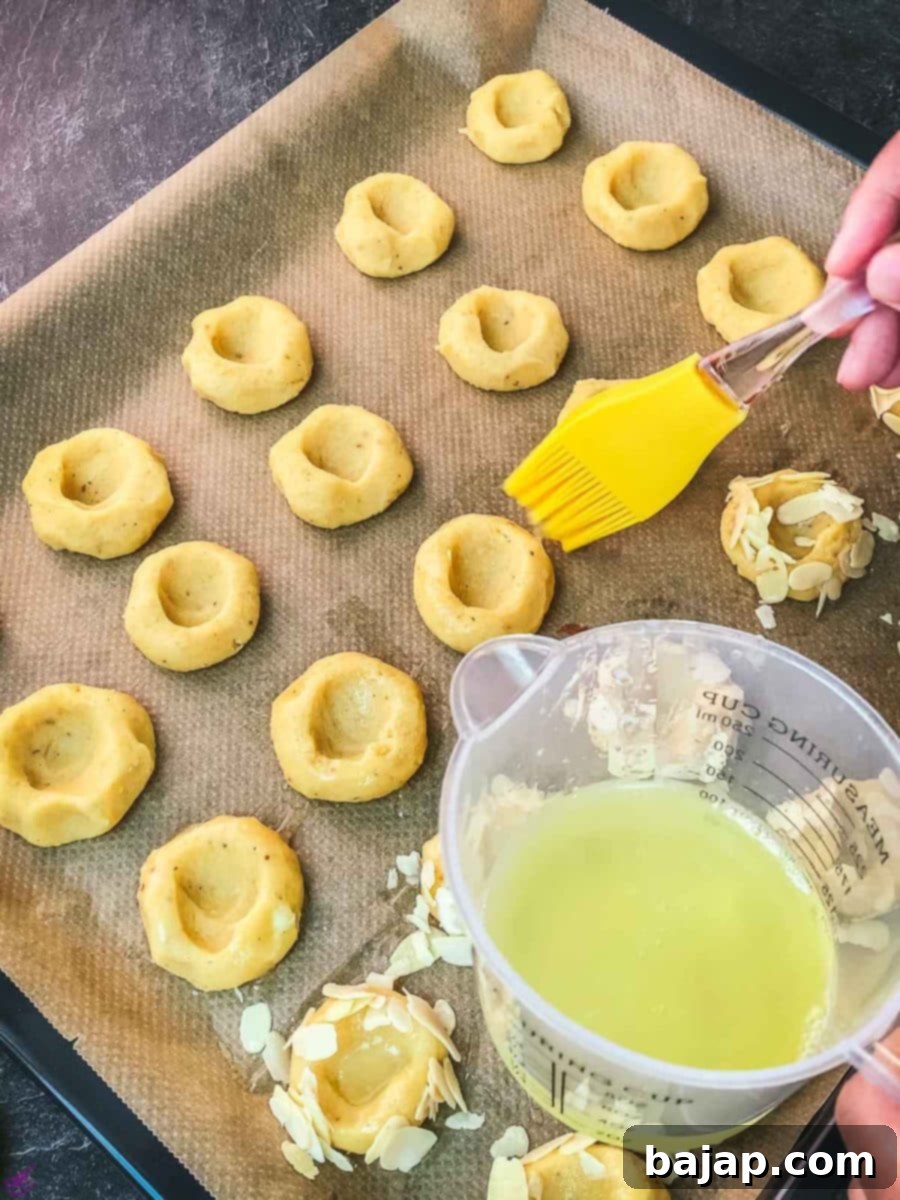 Brushing the formed cookie dough balls with egg white for a glossy finish and to help almond slivers adhere.
