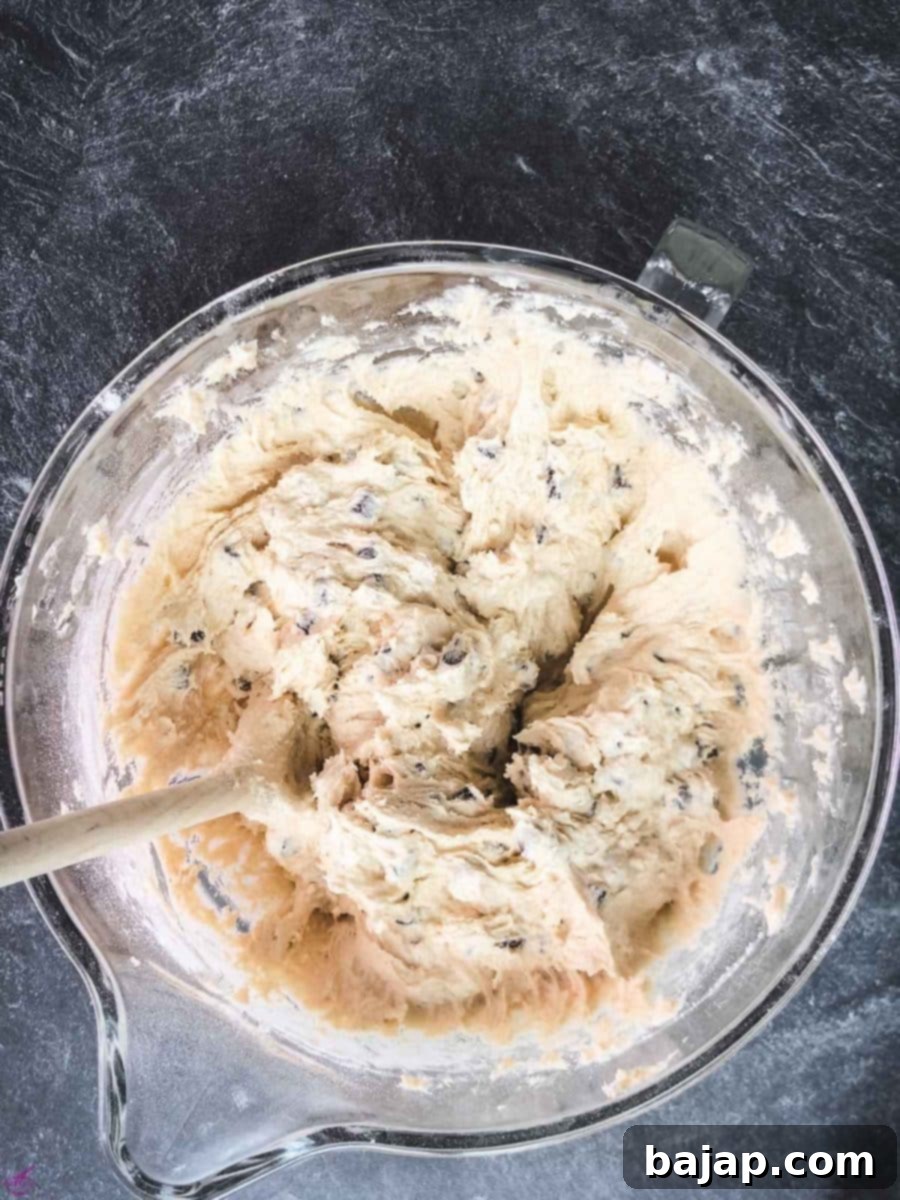 Mixing the dark chocolate chips thoroughly into the cookie dough using a wooden spoon.