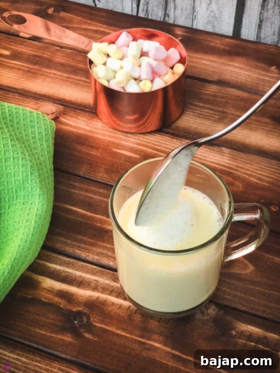 Adding a generous spoon of frothed white hot chocolate foam as a luxurious topping to the prepared drink in a glass cup.