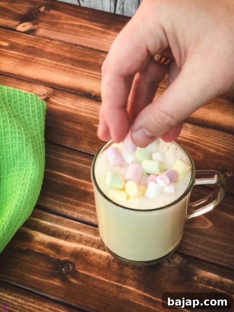 Garnishing the frothed white hot chocolate with a scattering of soft mini marshmallows, adding a sweet finish to the warm beverage.