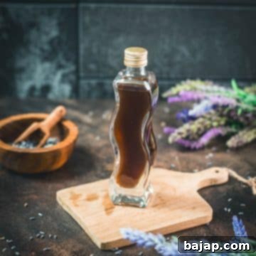 A beautiful curved bottle filled with homemade lavender extract, elegantly displayed on a brown wooden board, encircled by fresh lavender flowers, promising a fragrant culinary experience.