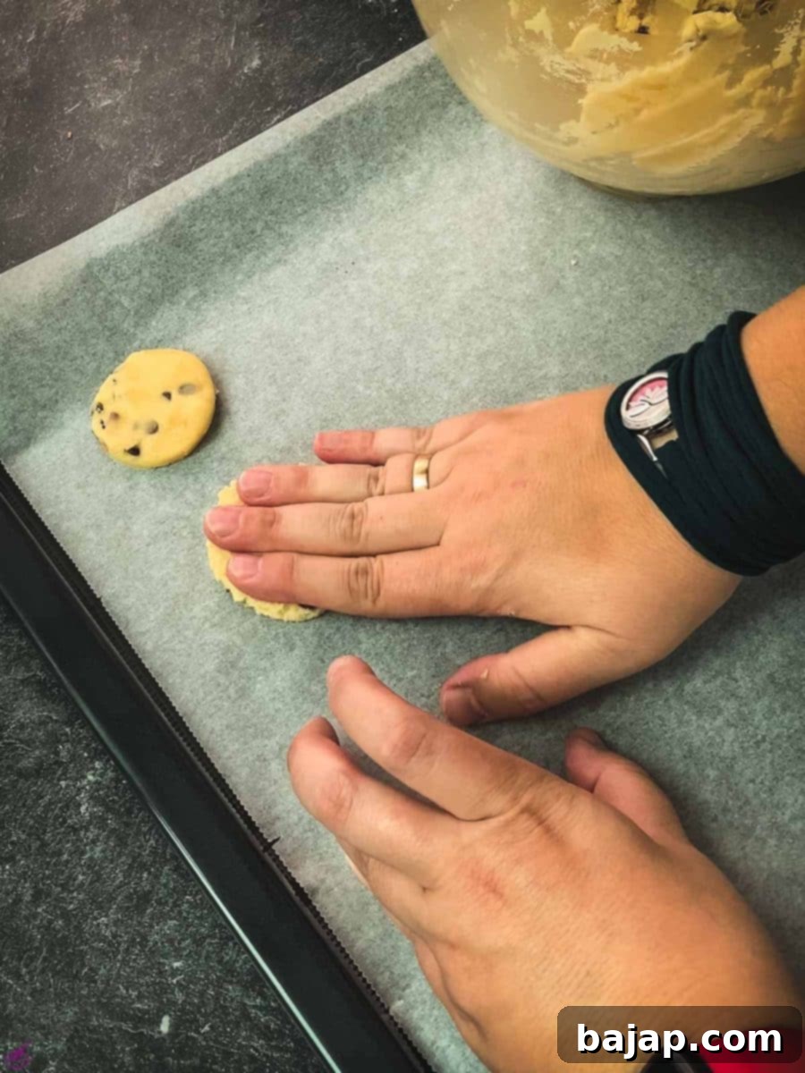Gently flatten the scooped cookie dough balls with your hand on the parchment-lined baking sheet, preparing them for cutting.