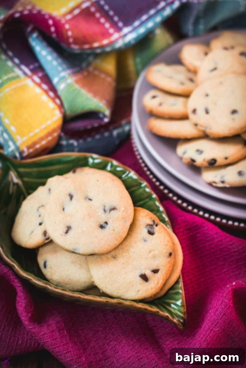 Beautifully baked chocolate chip sugar cookies placed on pink plates, carefully arranged among colorful tea towels, awaiting enjoyment with a glass of milk.