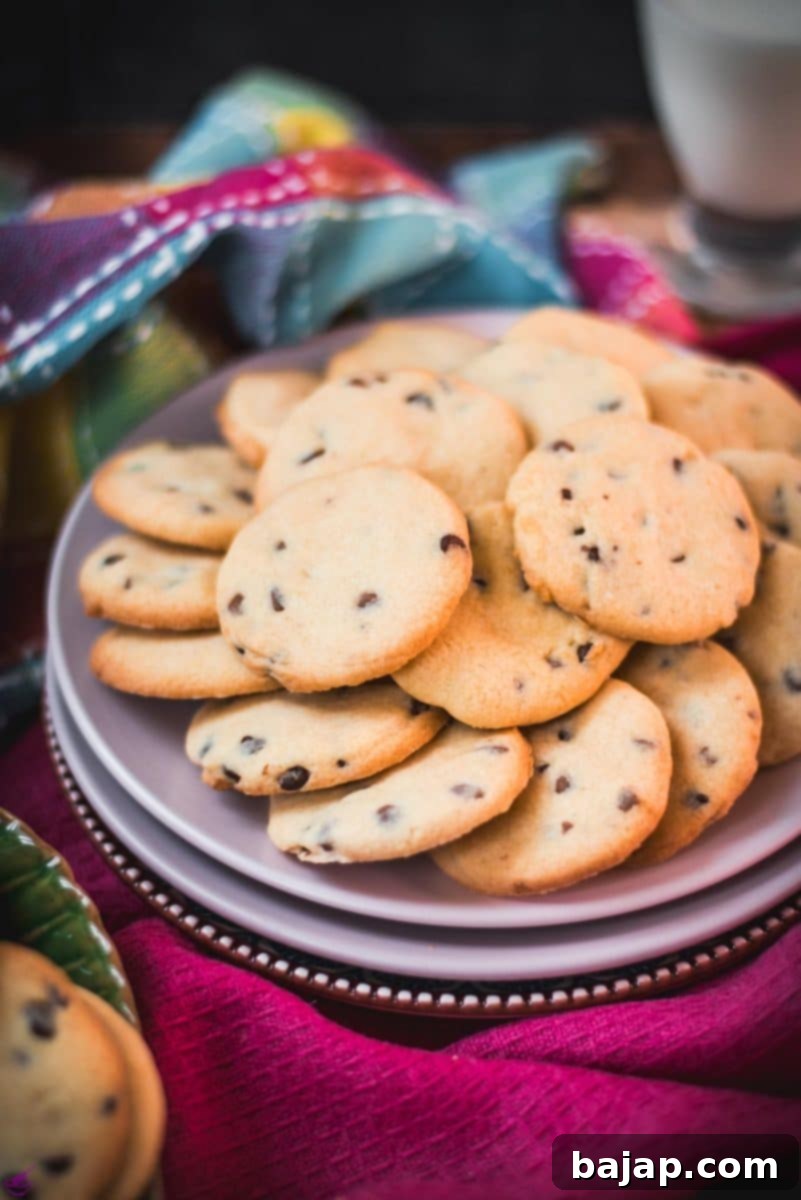 A delightful stack of chocolate chip sugar cookies placed on pink plates, with colorful tea towels and a glass of milk, perfectly presented for a sweet moment.