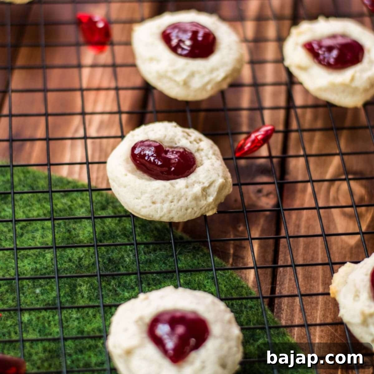 Gorgeous raspberry cream cheese thumbprint cookies on black cooling rack.