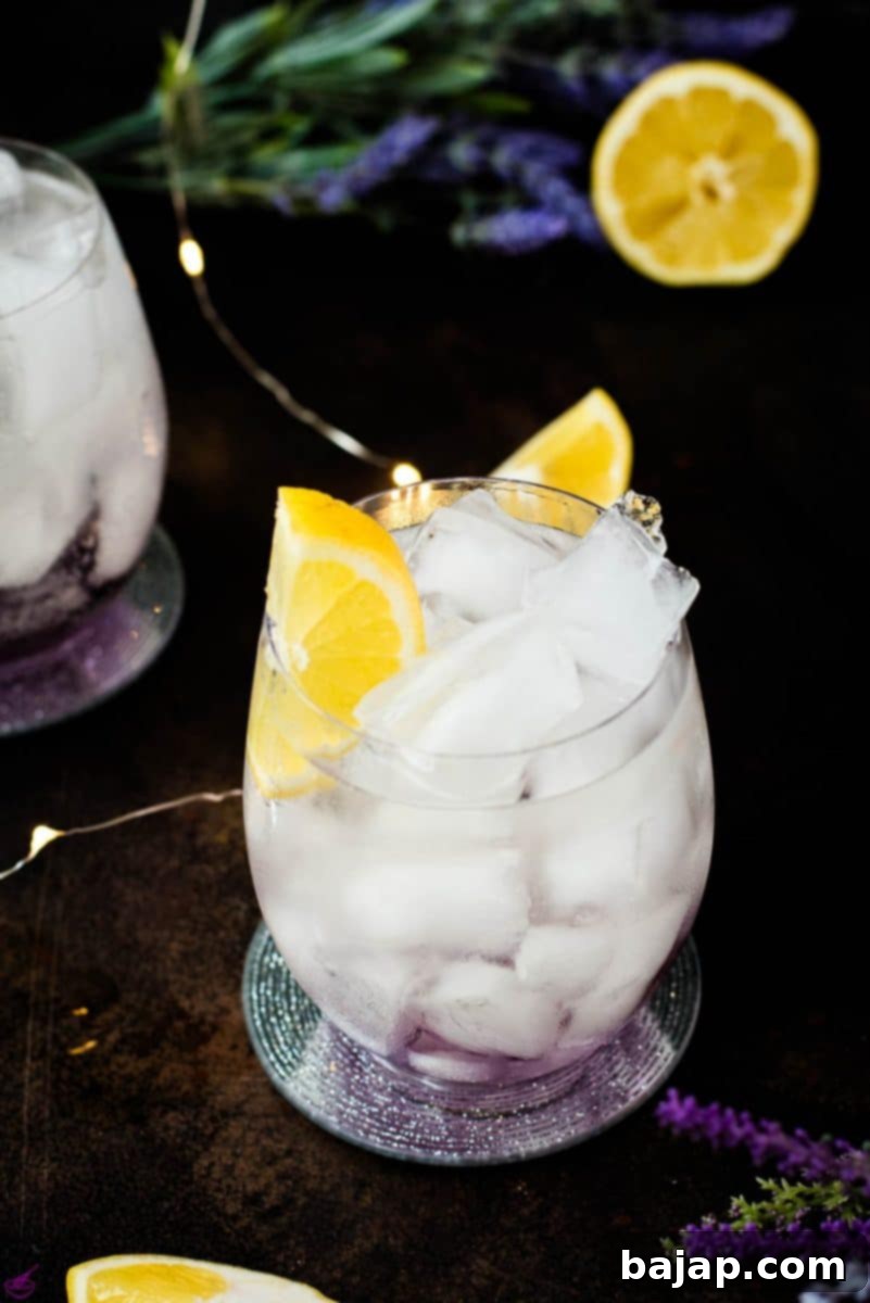 Gorgeous lavender spritz, garnished with lemon wedge and placed on shimmering coaster.