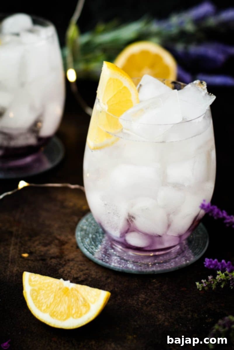 Gorgeous lavender spritz, garnished with lemon wedge and placed on shimmering coaster.