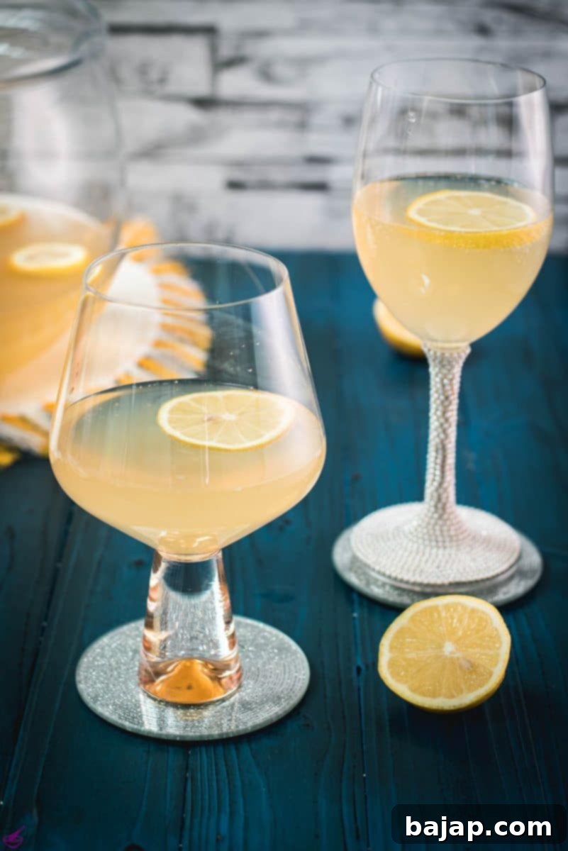 Sparkling Citrus Celebration 10 Two elegant glasses brimming with sparkling lemon punch, adorned with a vibrant lemon slice and a fresh mint sprig, exquisitely presented on a mirrored coaster, perfect for a festive occasion.