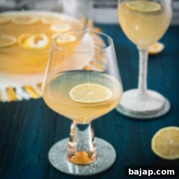 Sparkling Citrus Celebration 11 Two glasses elegantly filled with a bright yellow sparkling lemon punch, each garnished with a fresh lemon slice and a sprig of lemon balm, placed on a mirror coaster.