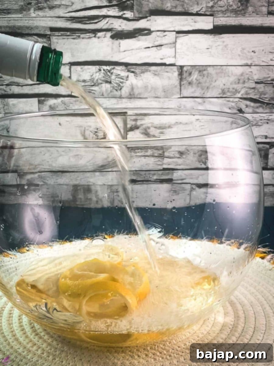 Sparkling Citrus Celebration 4 White wine being carefully poured into a glass punch bowl already containing vibrant lemon zest spirals, sitting on a clean white table mat to begin the infusion.