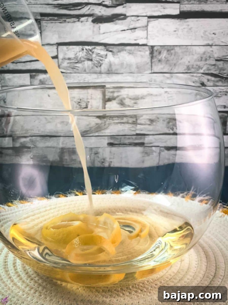 Sparkling Citrus Celebration 6 Freshly squeezed lemon juice being added to the punch bowl, which already holds infused white wine and lemon zest, on a white table mat.