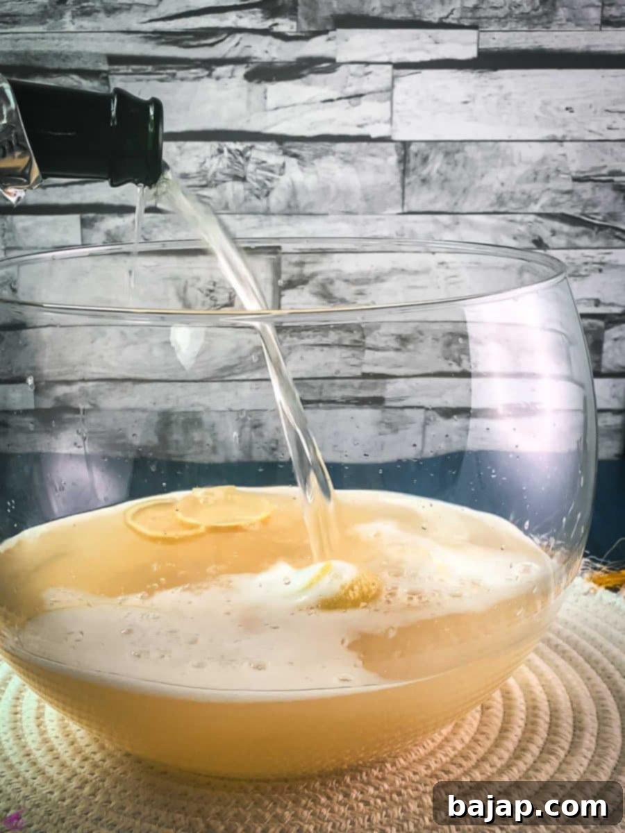 Sparkling Citrus Celebration 7 Sparkling wine is gently poured into a glass punch bowl, mixing with white wine, lemon juice, and zest on a white table mat, creating the signature fizz.