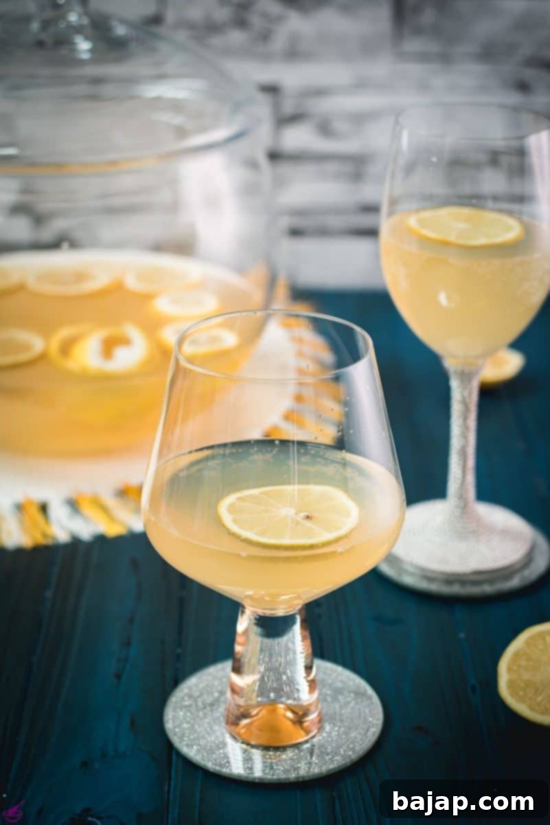 Sparkling Citrus Celebration 9 Two beautifully presented glasses filled with Sparkling Lemon Punch, each adorned with a fresh lemon slice and delicate lemon balm, artfully placed on a mirrored coaster, creating a festive and inviting scene.